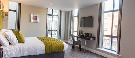 Habitación de hotel con cama, escritorio y ventanas amplias.
