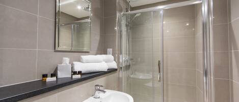 A modern bathroom with a glass-enclosed shower, a white sink, and a mirror above the counter.