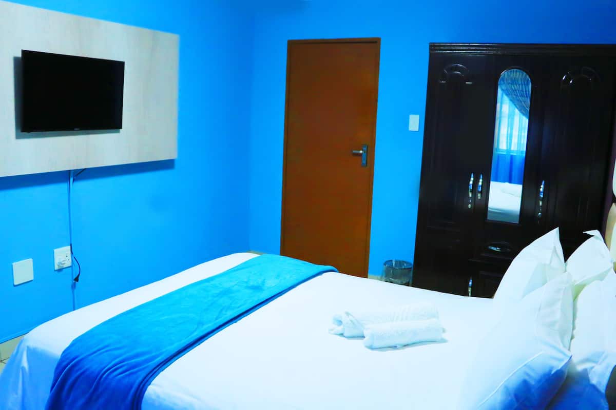 A hotel room with a bed, a television mounted on the wall, a door, and a mirror reflecting a bed.