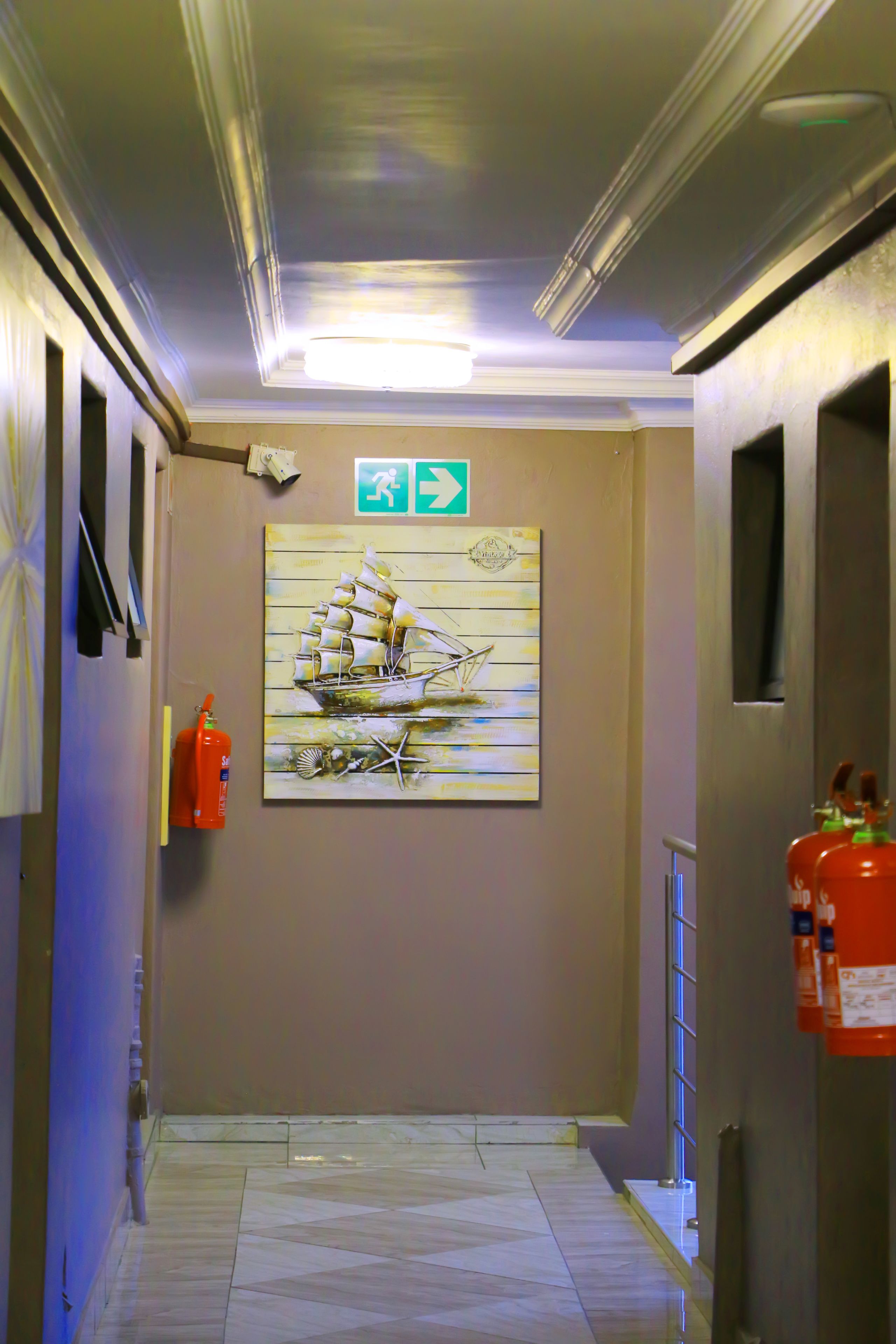 Ein Flur mit Fliesenboden, einem Gemälde eines Segelschiffs und Feuerlöschern an beiden Seiten.