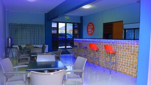 A clean, modern indoor space with a seating area featuring tables and chairs, a brick accent wall, and a sign indicating free WiFi. - Angel Guest House (Johannesburg)