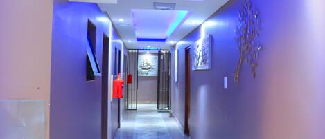 A modern hallway with a polished tile floor, recessed lighting, and a fire extinguisher mounted on the wall.