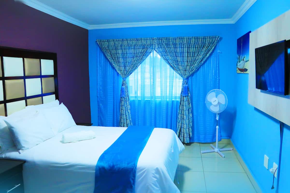 A hotel room with a bed, curtains, a fan, and a TV on the wall.