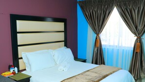 A hotel room with a large bed, a nightstand, and a window with curtains. - Angel Guest House (Johannesburg)
