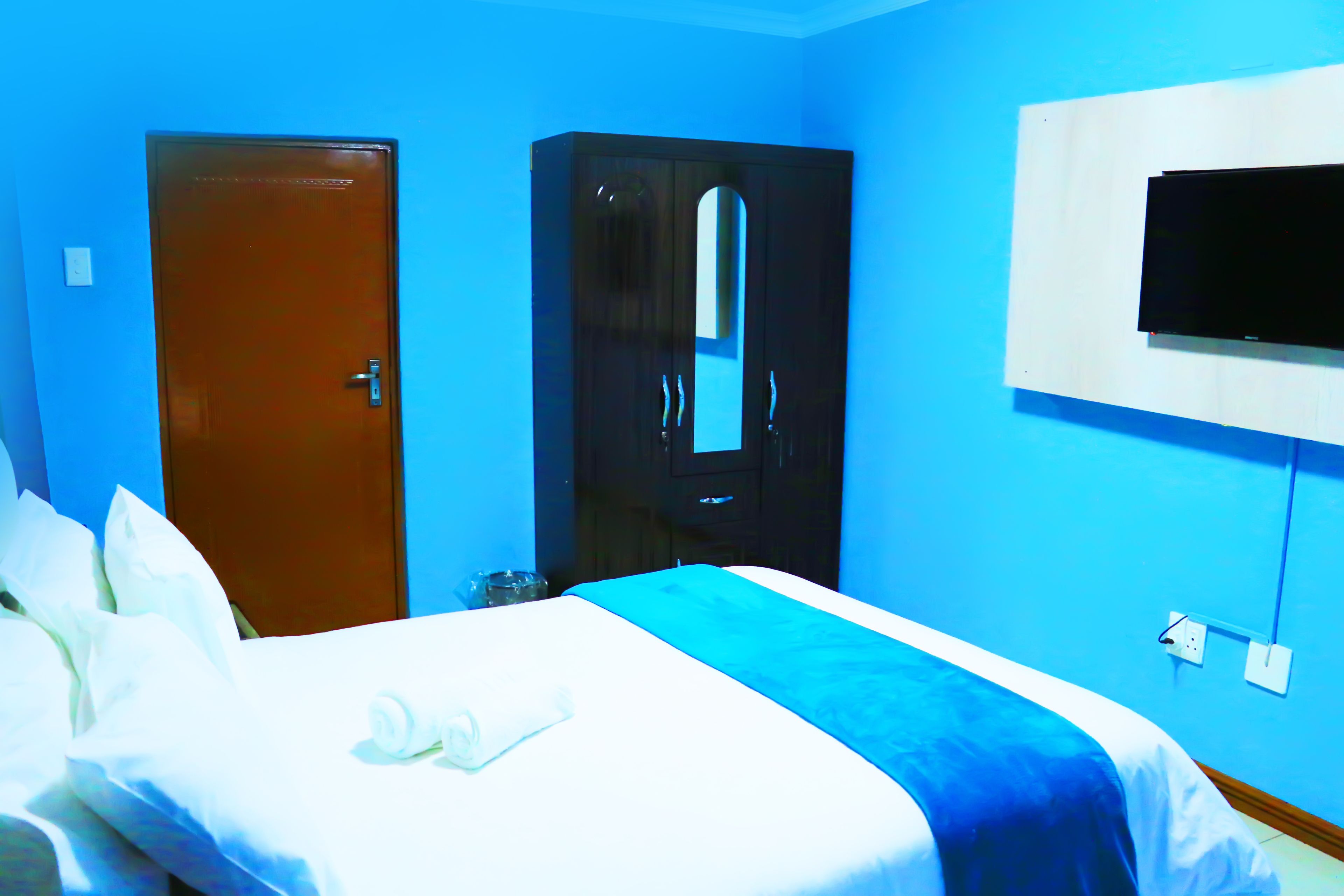 Quarto de hotel com uma cama, um guarda-roupa e uma televisão fixada na parede.