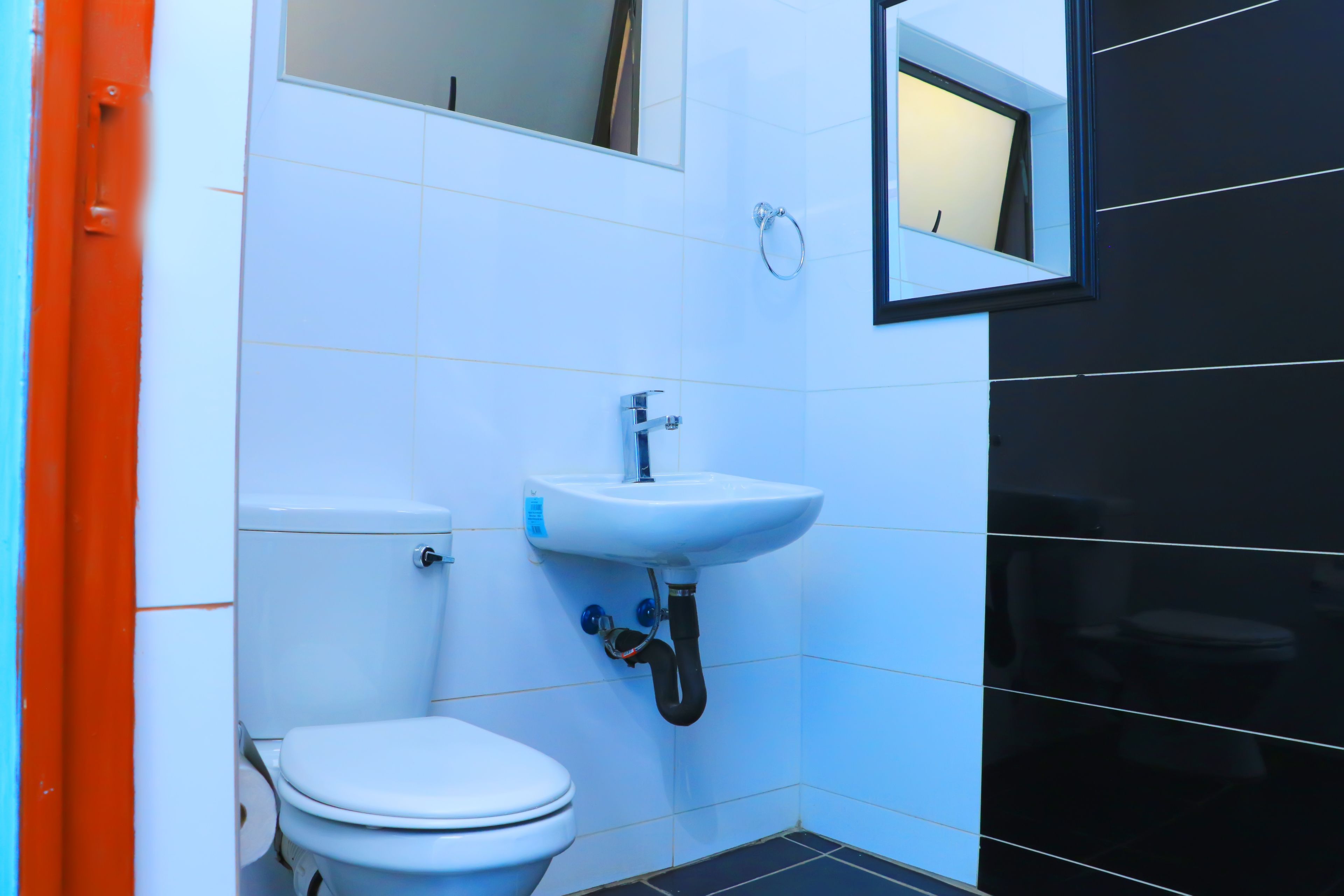 A small, modern bathroom with white and black tiles, a white toilet, a white sink with a mirror above it, and a red door.