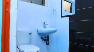 A small, modern bathroom with white and black tiles, a white toilet, a white sink with a mirror above it, and a red door.