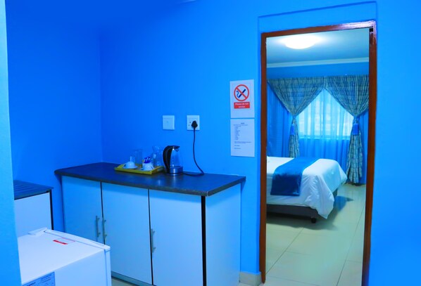 Una habitación de hotel con cama, escritorio con hervidor y pared azul.