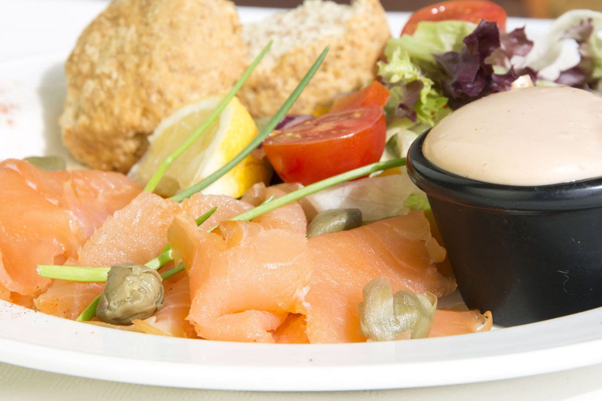 A plate with smoked salmon, capers, lemon, and a small bowl of sauce.