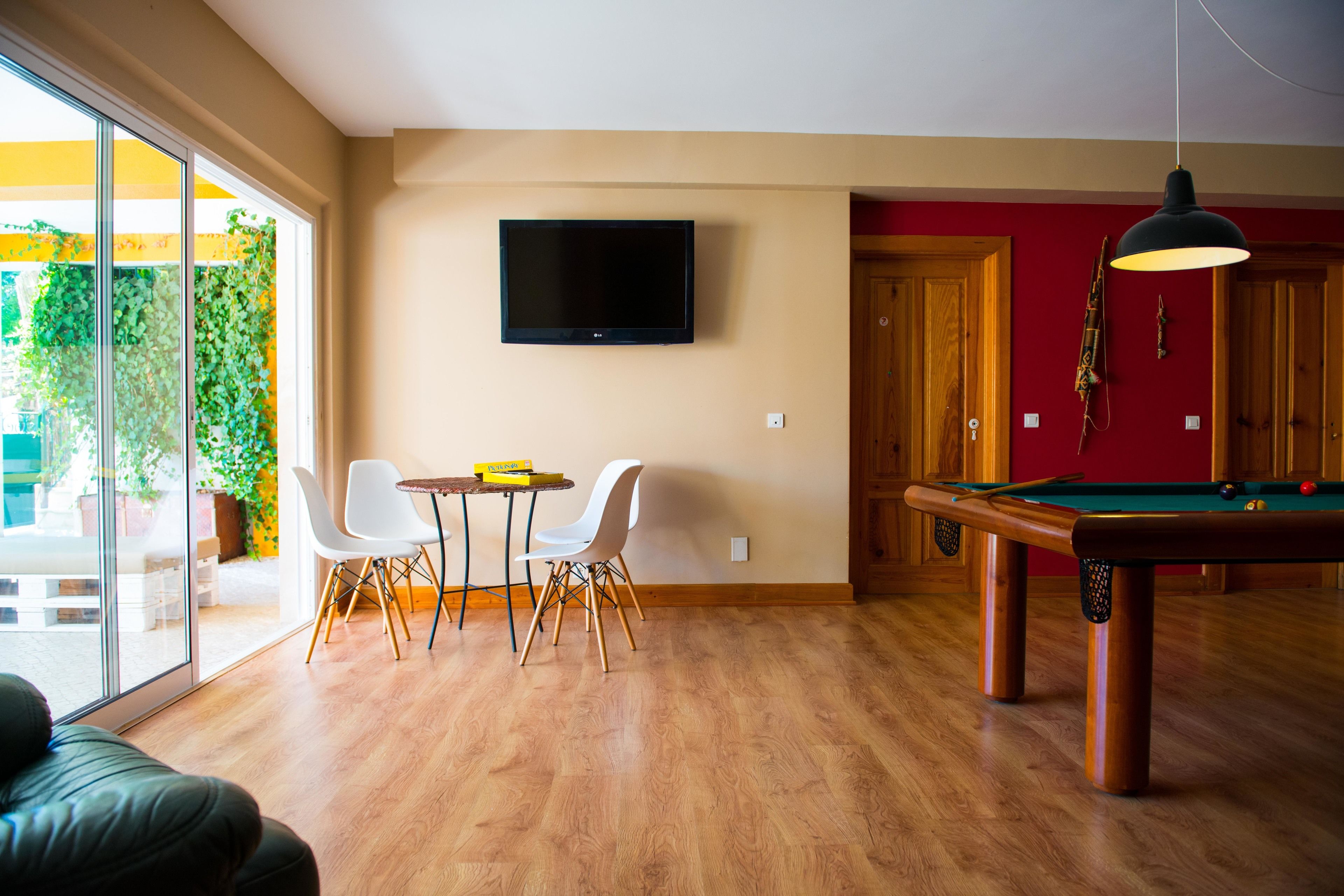 Un salon comprenant une table de billard, un téléviseur fixé au mur et un coin repas avec deux chaises et une table.