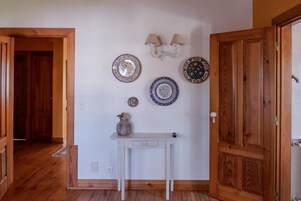 Un pasillo con una mesa blanca, platos decorativos y una puerta de madera.