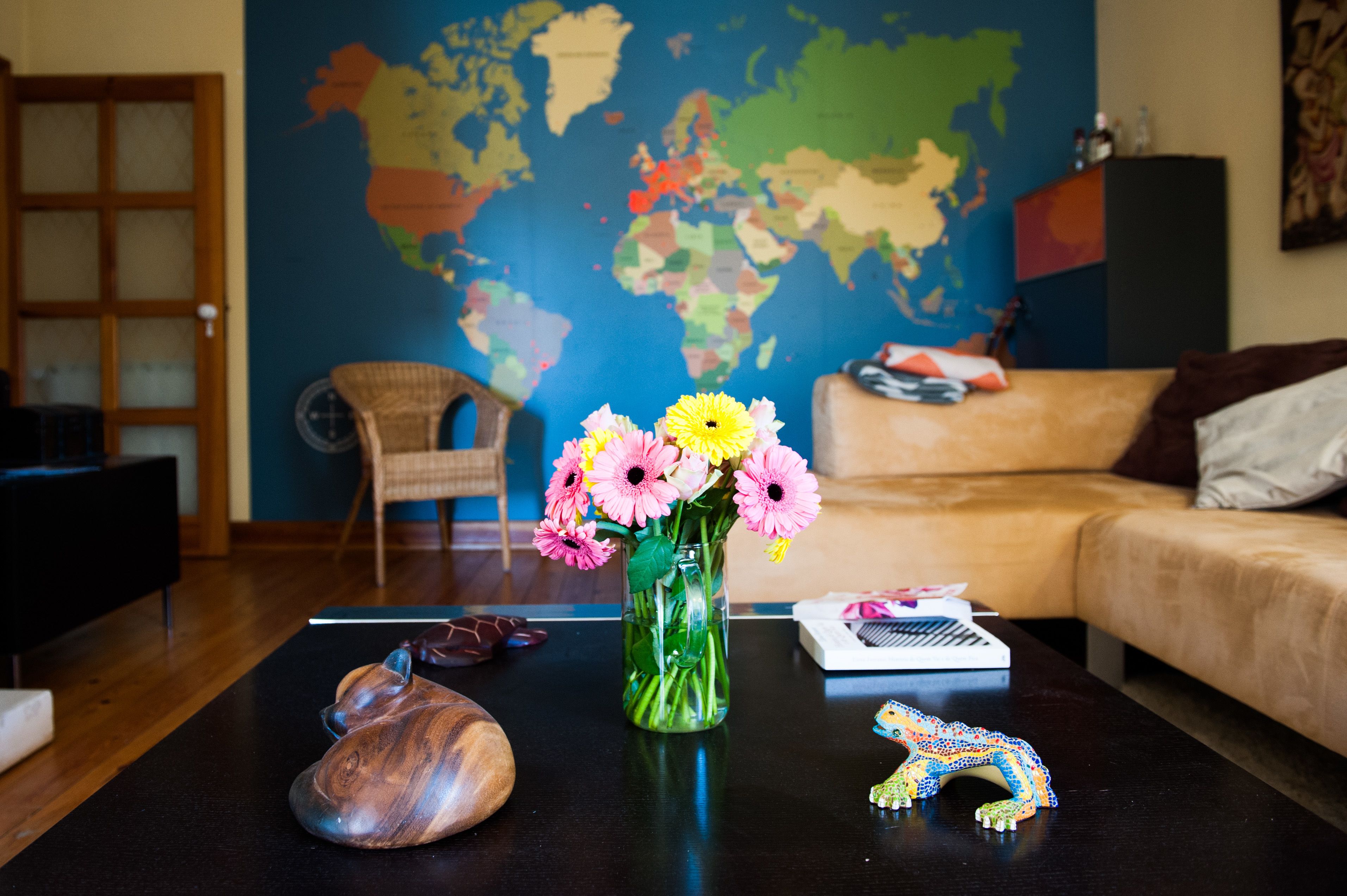 Uma sala de estar com um mapa-múndi na parede, uma mesa de centro com um vaso de flores, uma escultura de madeira e um brinquedo.