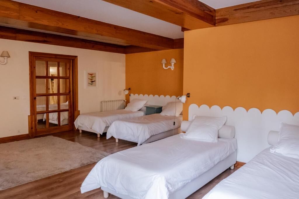 A room with three single beds, a wooden ceiling, a door with glass panels, and a wall-mounted light fixture.