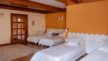 A room with three single beds, a wooden ceiling, a door with glass panels, and a wall-mounted light fixture.