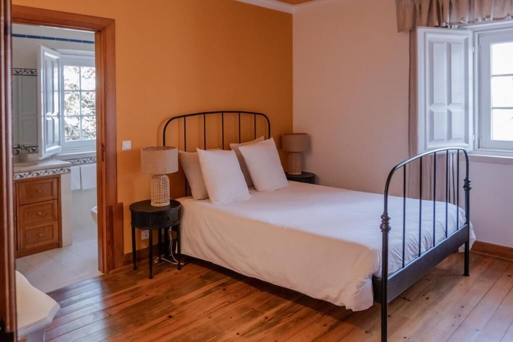 A bedroom with a metal bed frame, a bedside table with a lamp, and a window with curtains.
