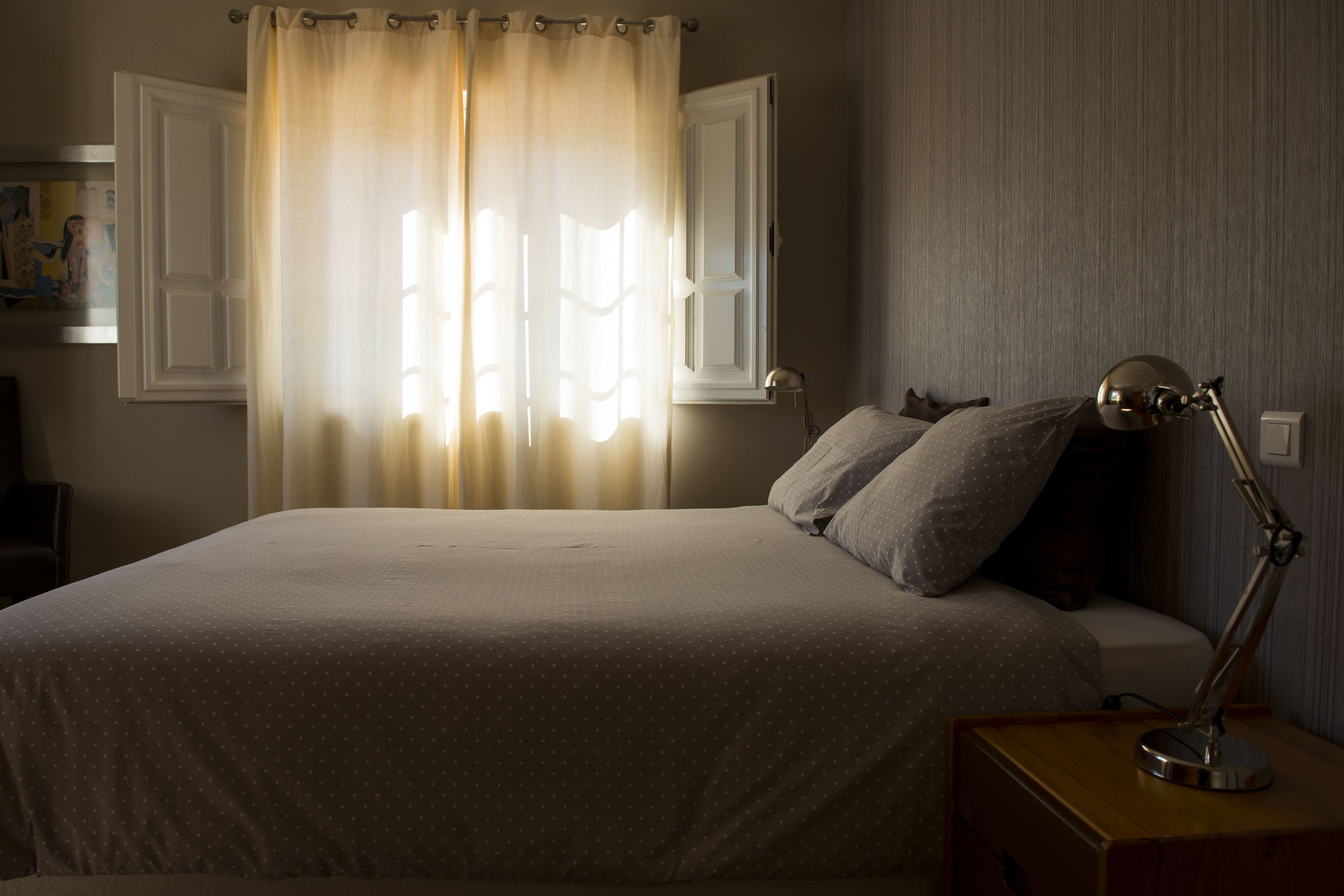 Cama bem arrumada com almofada e mesa de cabeceira com abajur.