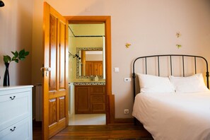 A bedroom with a wooden door leading to a bathroom, a bed with white bedding, and a dresser with drawers. - Magnolia B&B (Leiria)