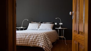 Een slaapkamer met een geruite sprei, twee nachtkastjes met lampen en een donkere muur.