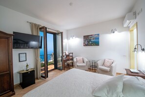 Een slaapkamer met een bed, televisie, bureau, stoel en een balkon met uitzicht.