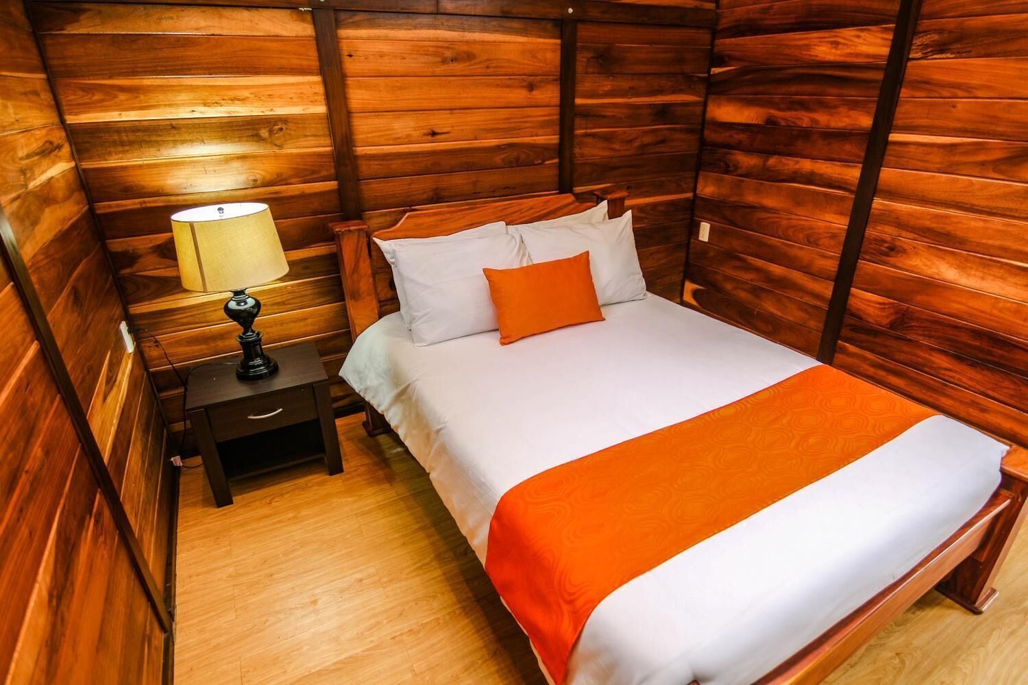 A wooden-paneled room with a bed, a nightstand, and a lamp.