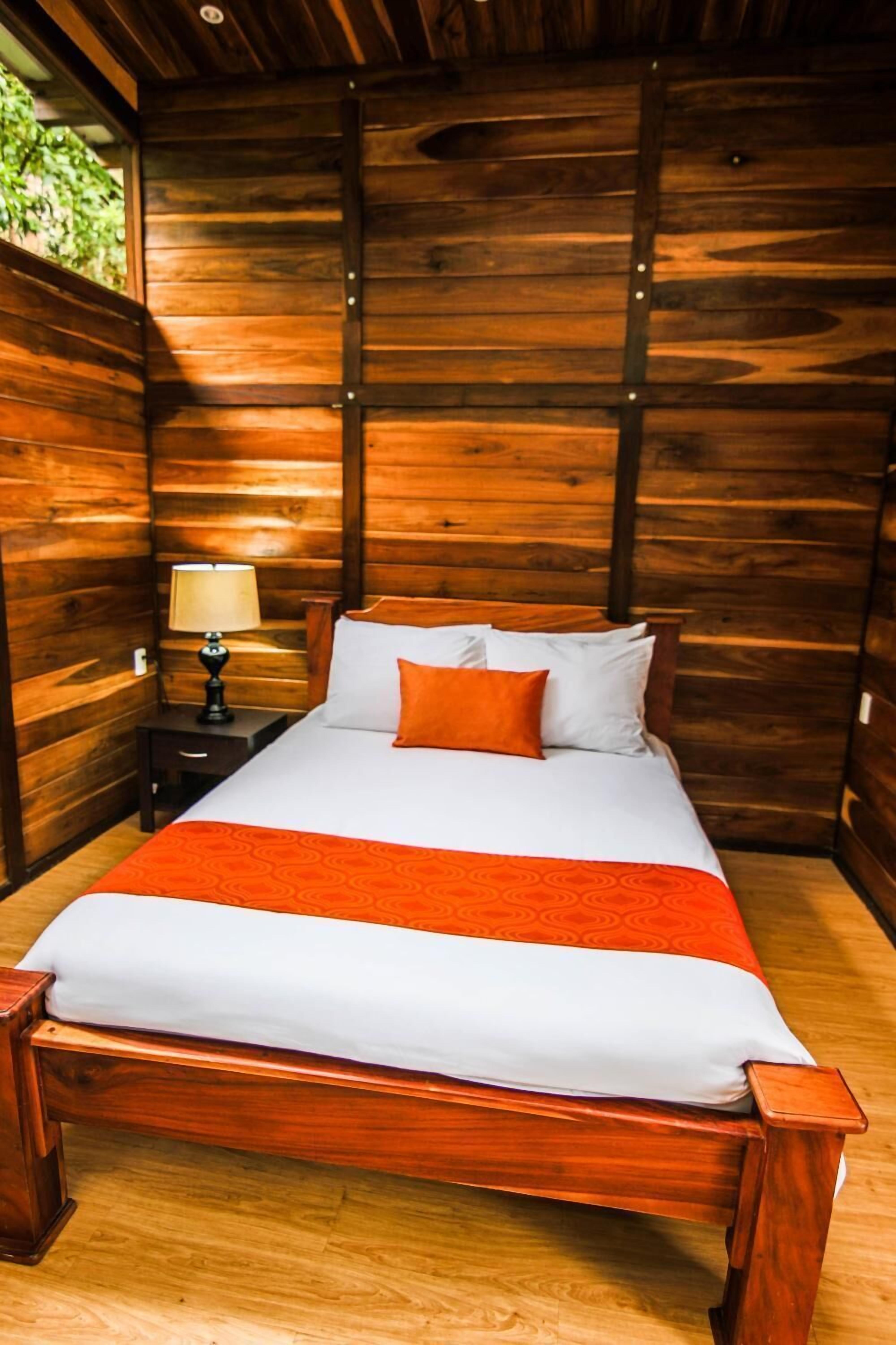 A wooden-paneled room with a bed, a nightstand, and a lamp.