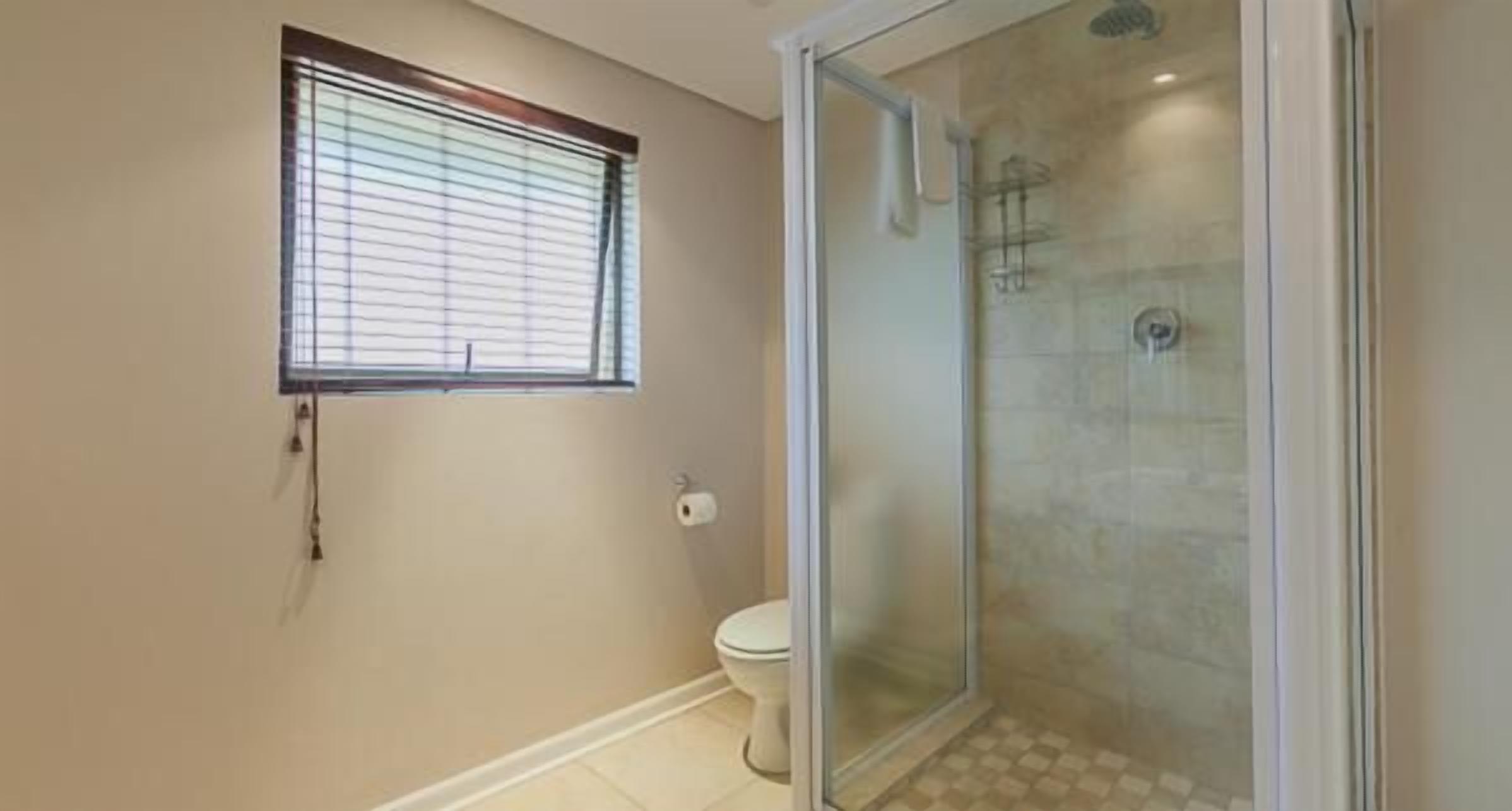 A bathroom with a toilet, a shower with a glass door, and a window with blinds.