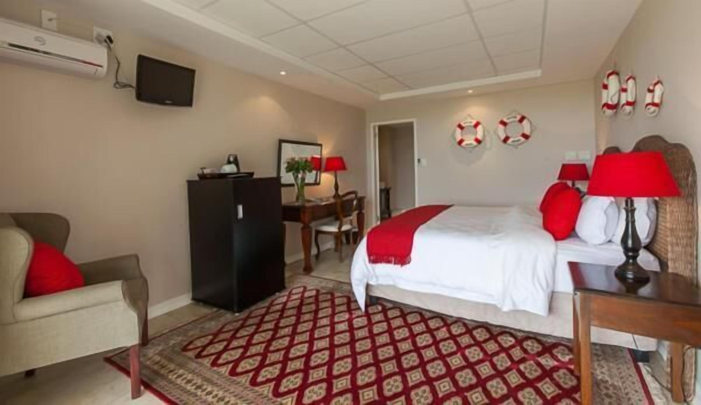 A hotel room with a bed, a desk, a chair, a television, and a patterned rug.