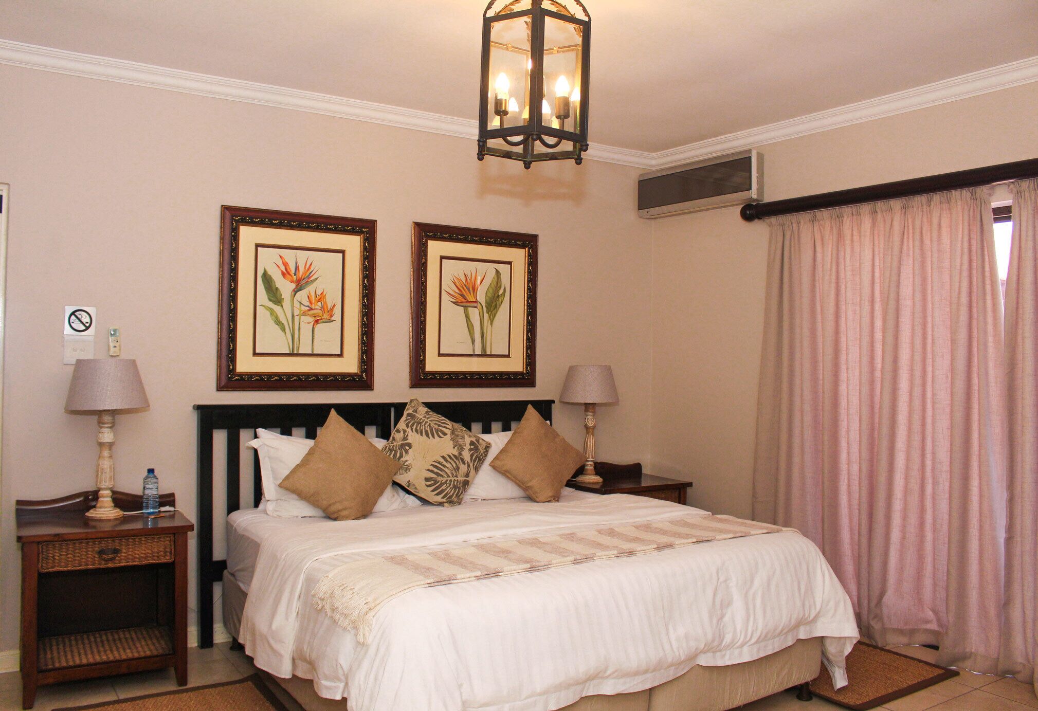 A hotel room with a bed, two nightstands, a lamp on each, a framed picture on the wall, and a window with curtains.