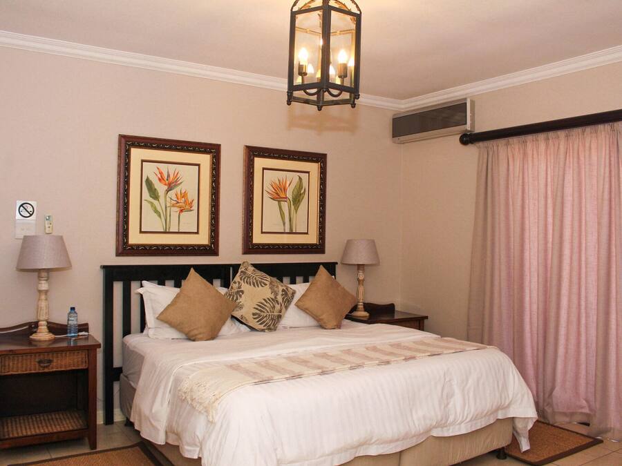 A hotel room with a bed, two nightstands, a lamp on each, a framed picture on the wall, and a window with curtains.