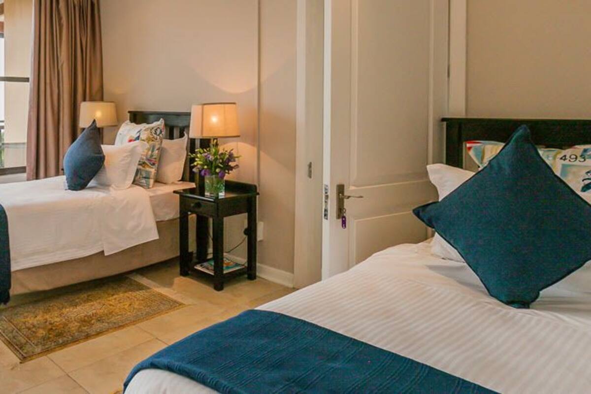 A hotel room with two beds, a balcony, and a view of greenery.