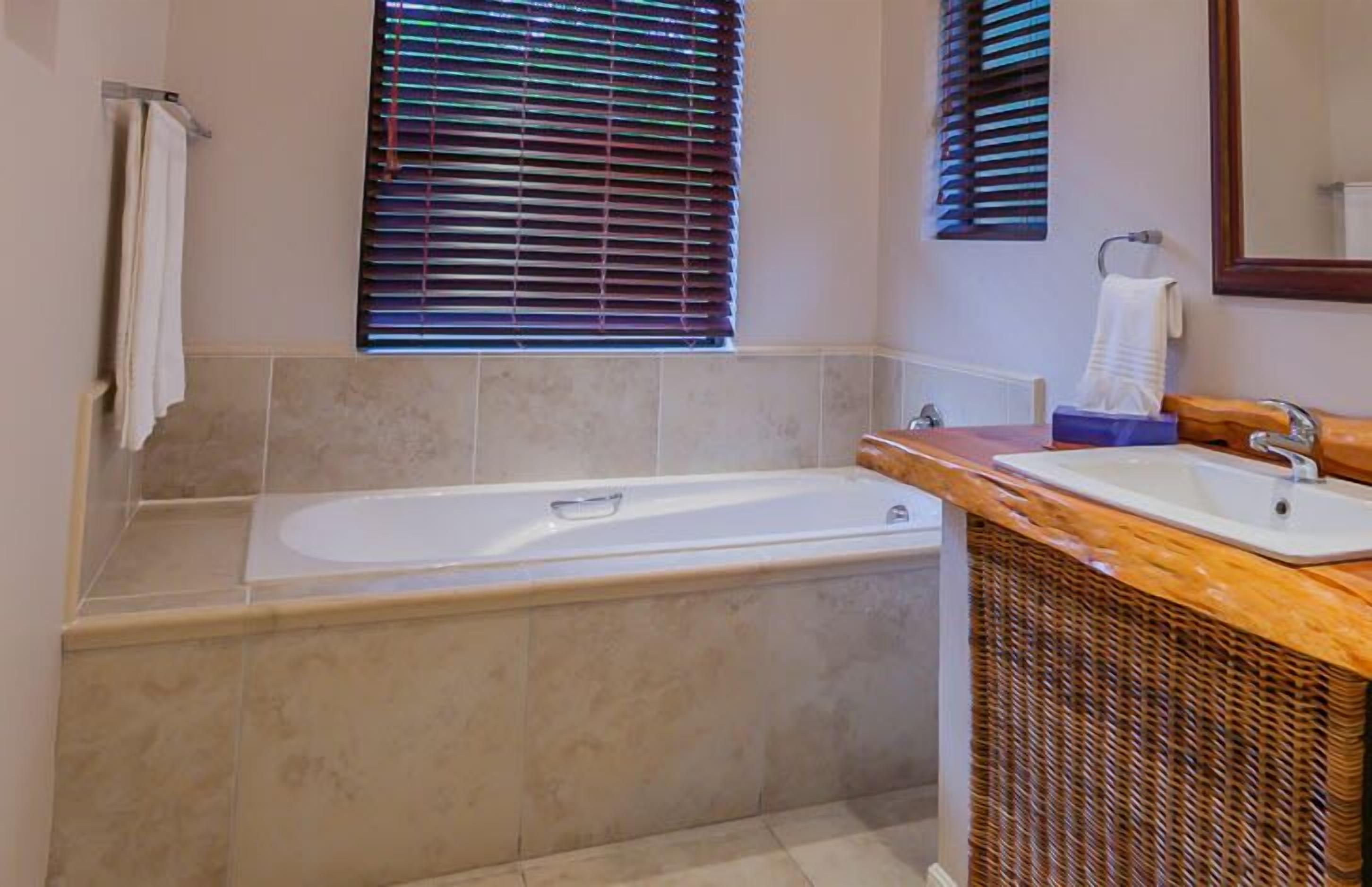 A bathroom with a bathtub, a sink, and a window with blinds.