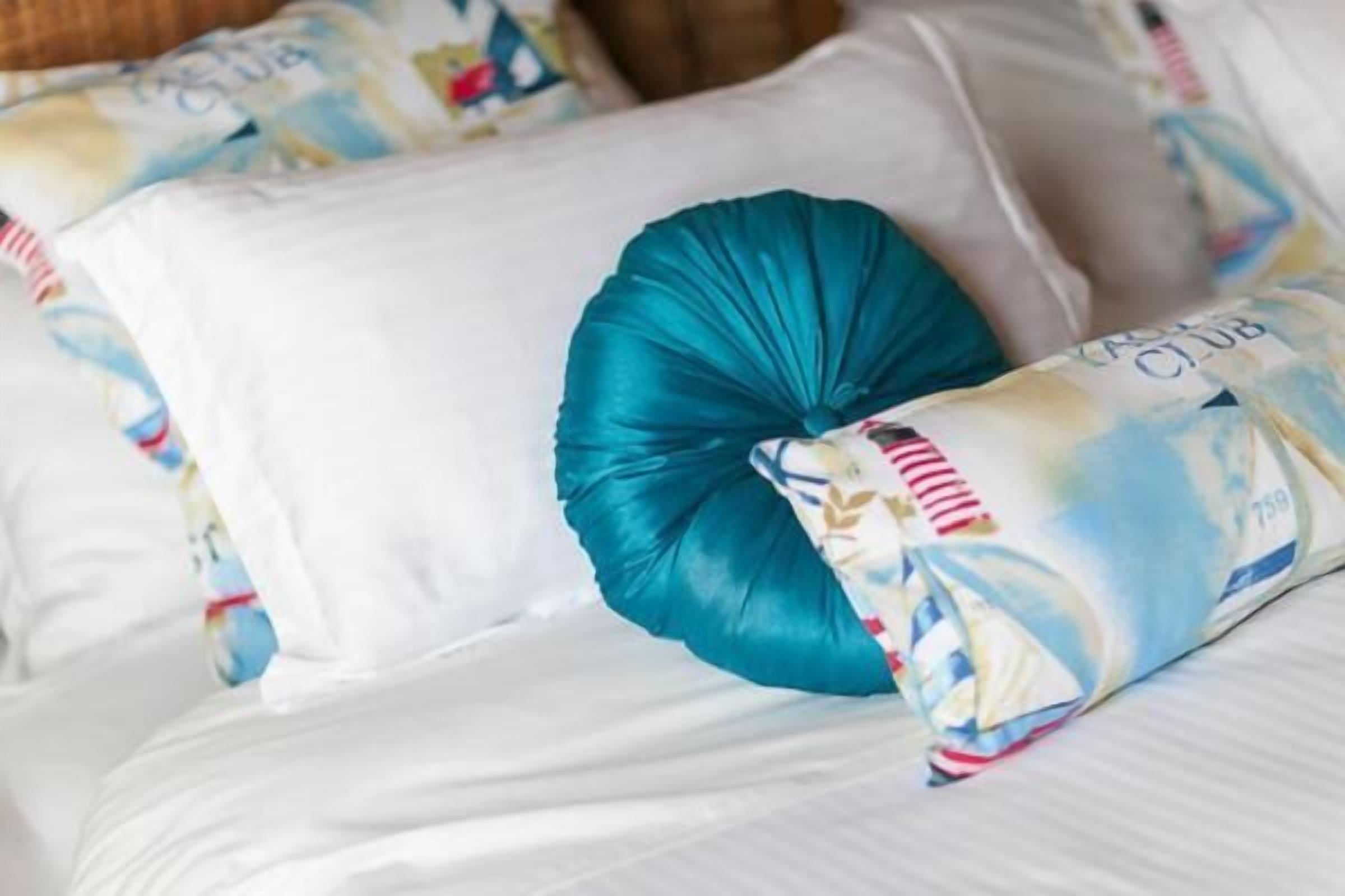 Un lit avec une literie blanche et un coussin décoratif de couleur turquoise.