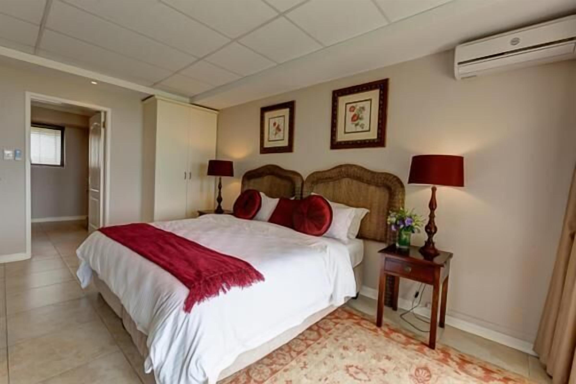 A bedroom with a bed, two bedside tables, a nightstand, a wall-mounted air conditioner, and a door leading to another room.