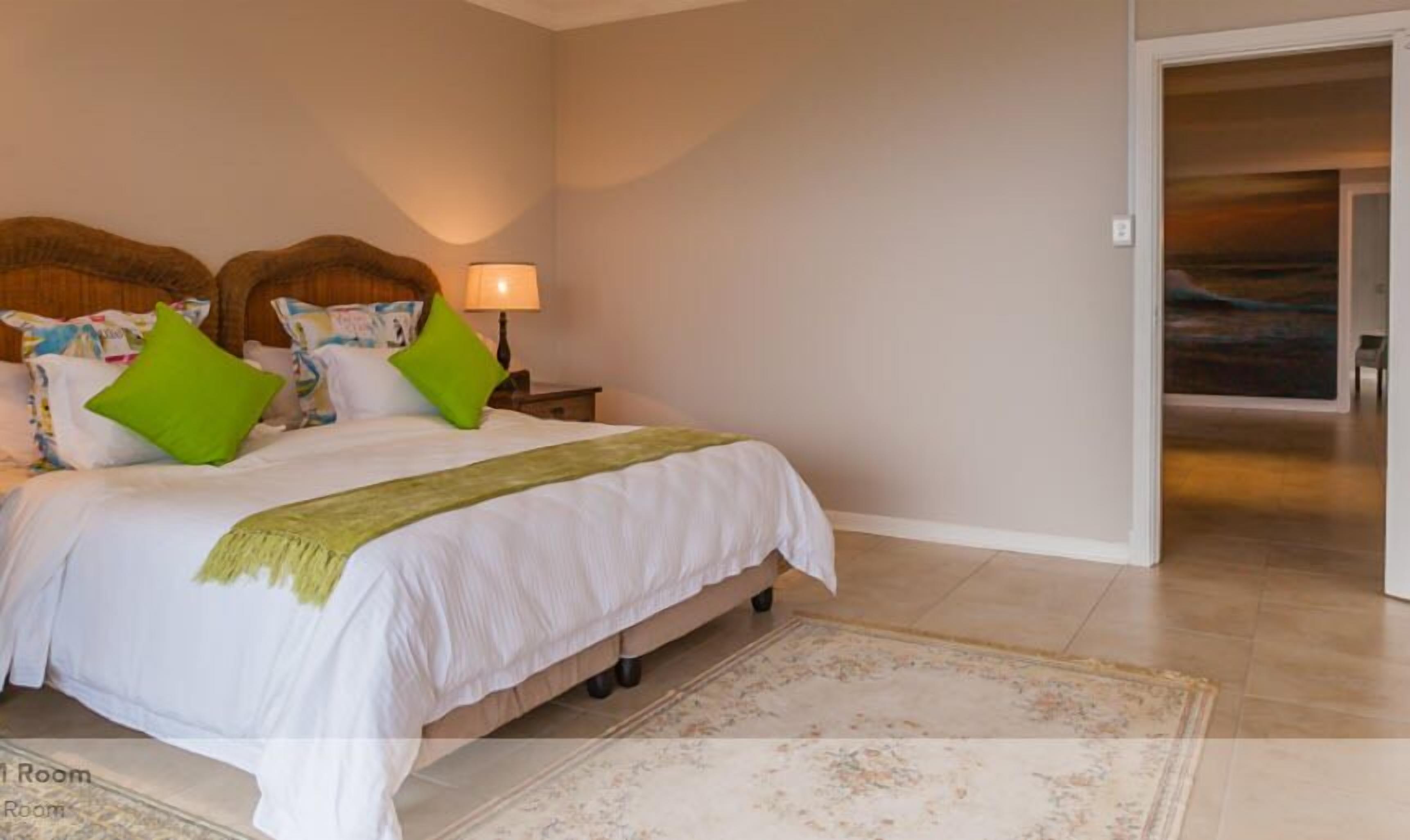 A bedroom with a bed, pillows, a nightstand, a lamp, and a view of the ocean through a door.