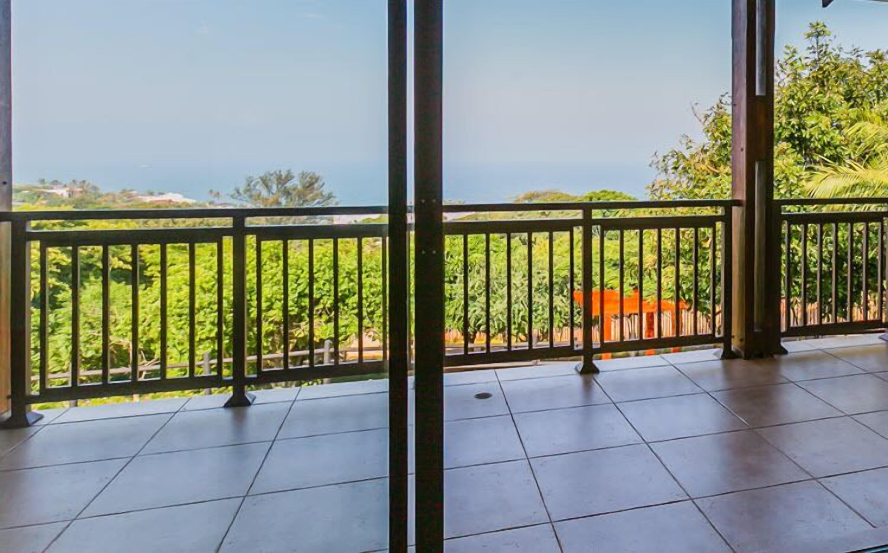 A balcony with a view of a lush garden and a distant building.