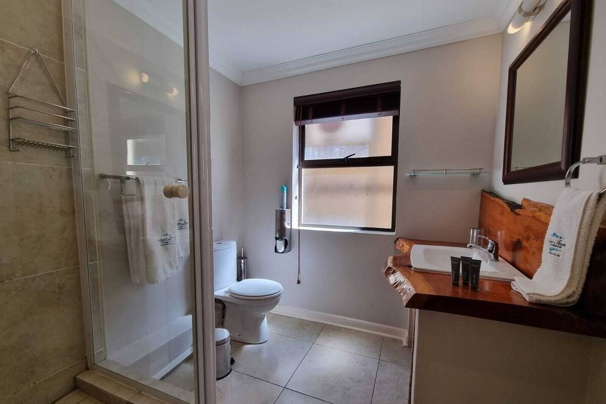 A modern bathroom with a glass shower enclosure, a toilet, and a sink area with toiletries.