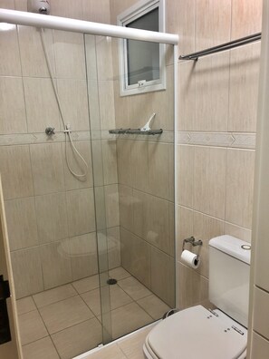 A modern bathroom with a glass-enclosed shower, a toilet, and a window above the sink. - Condomínio Residencial Grand Beach (Ubatuba)