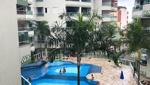 A residential building with a swimming pool surrounded by palm trees and a stone patio. - Condomínio Residencial Grand Beach (Ubatuba)
