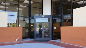 A modern building entrance with a revolving door, glass facade, and a visible car parked outside. - Red Carpet Inn (Macon)