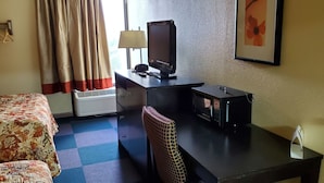 A hotel room with a bed, a desk with a television, a chair, a lamp, and a framed picture on the wall. - Red Carpet Inn (Macon)