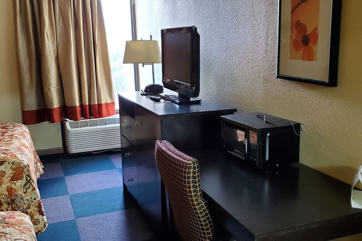 Ein Hotelzimmer mit Bett, Schreibtisch mit Fernseher, Stuhl, Lampe und einem gerahmten Bild an der Wand.