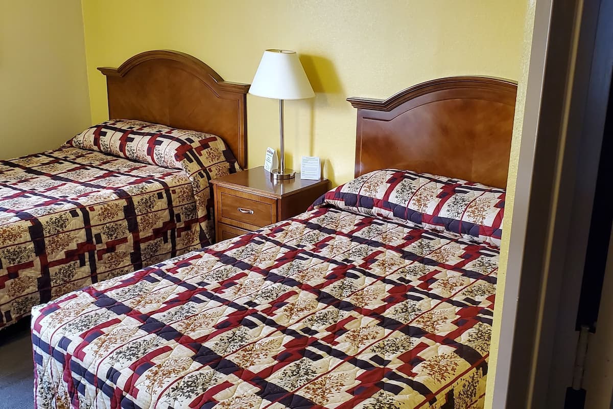 Ein Hotelzimmer mit zwei Betten, jeweils mit einem gemusterten Überwurf, einem Nachttisch mit Lampe und einem gerahmten Bild an der Wand.