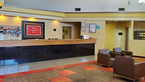A reception area with a reception desk, framed sign, chairs, and a carpeted floor. - Red Carpet Inn (Macon)