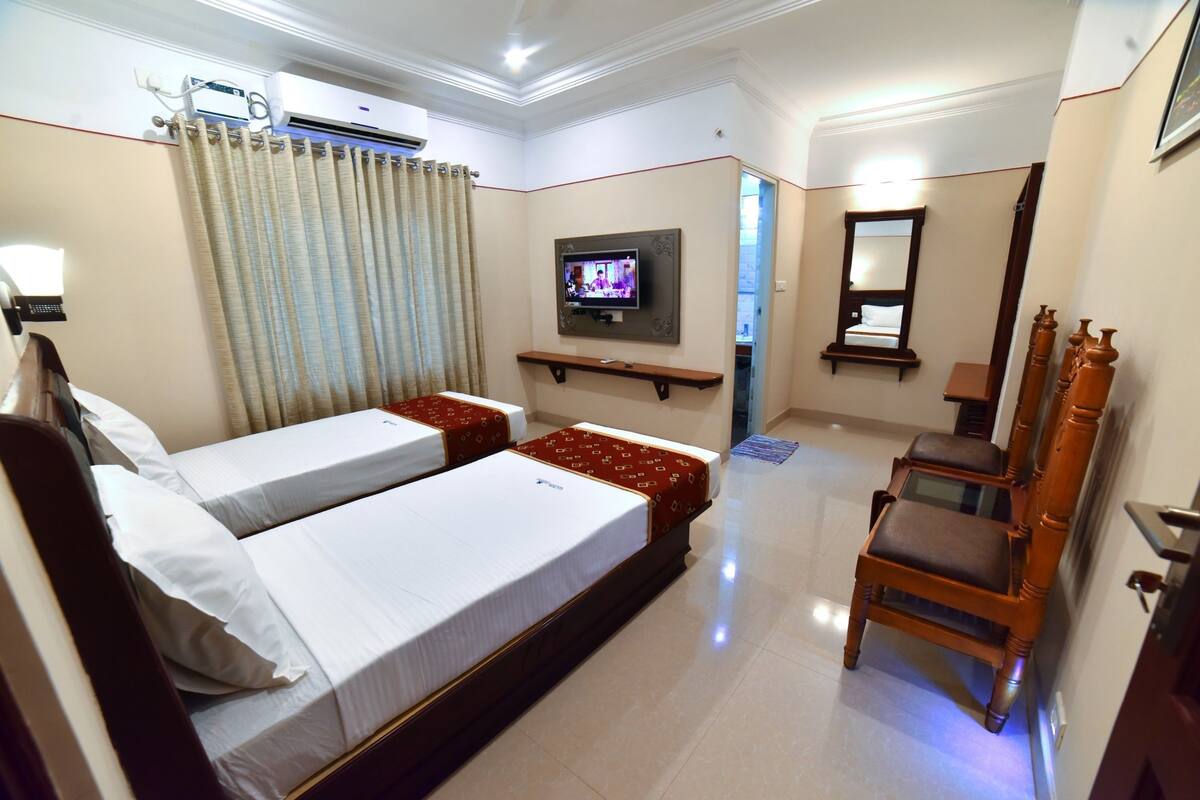 A hotel room with two beds, a TV, a chair, and a mirror.
