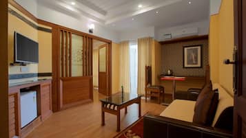 Una habitación de hotel con suelo de madera, un sofá, una mesita, un televisor, un escritorio y una cama.