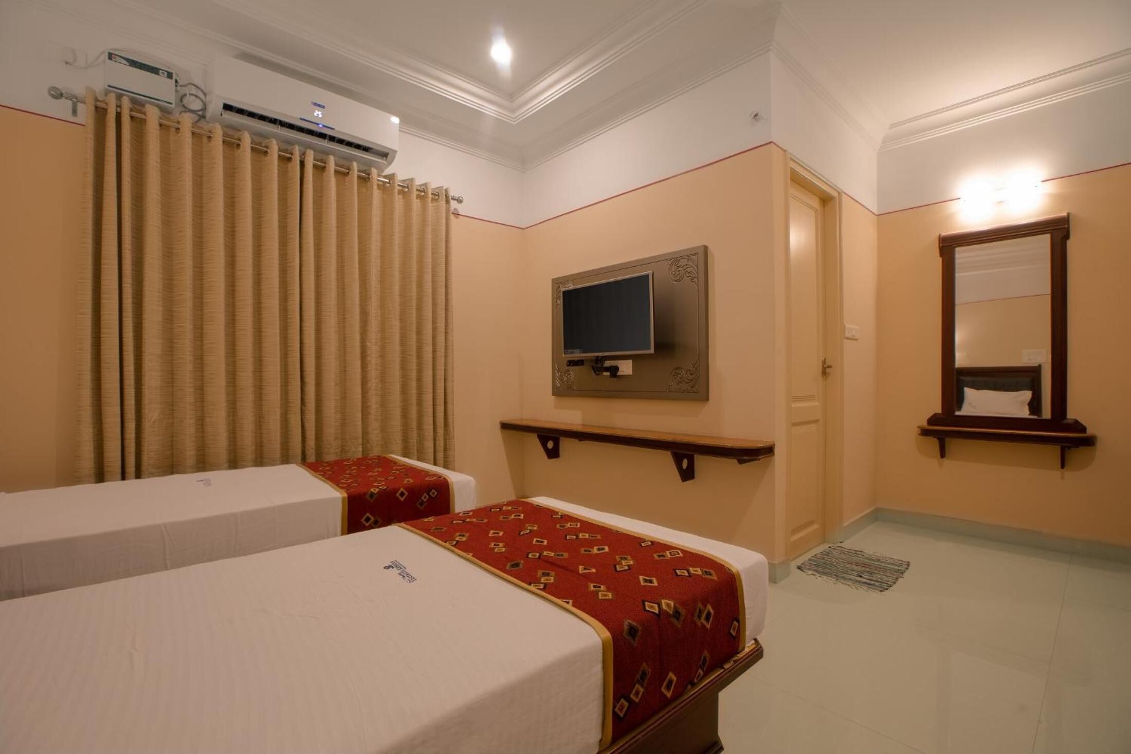 A hotel room with two beds, a television, a mirror, and a window with curtains.
