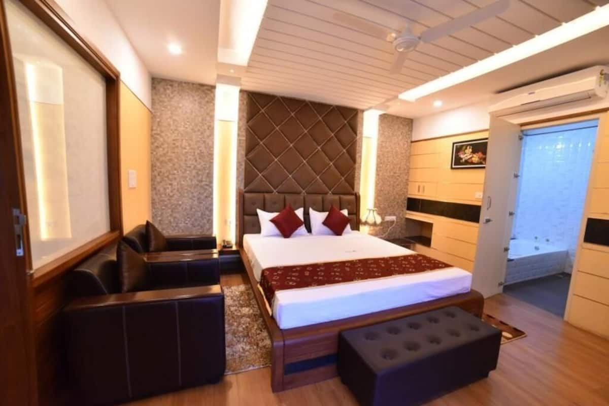 A hotel room with a large bed, a seating area, a wardrobe, and a door leading to a bathroom.