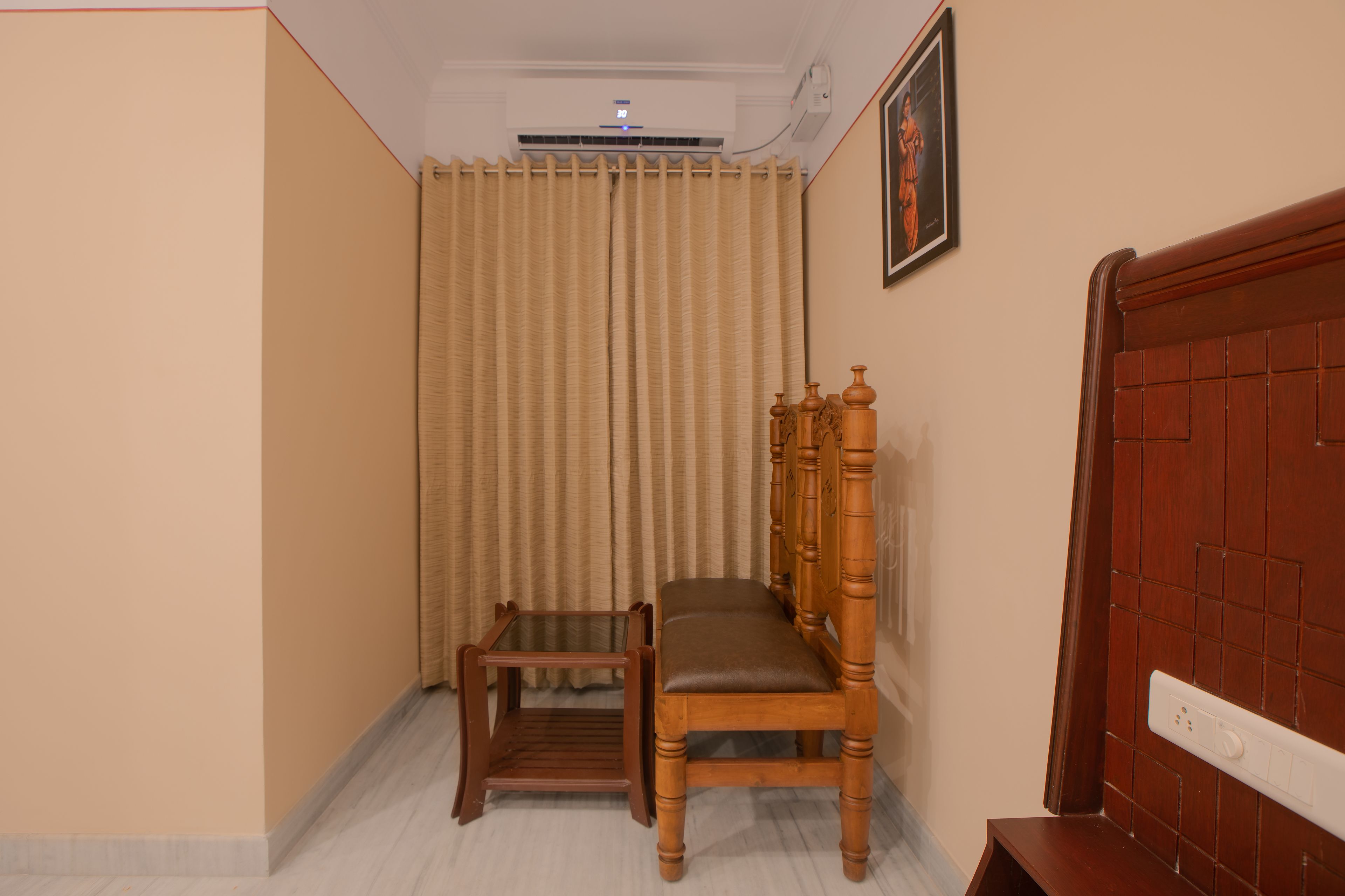 Una habitación con una silla de madera, una mesita pequeña, un ventilador de techo y un interruptor de luz en la pared.