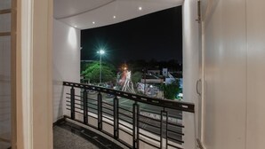 Un balcón con vista a una calle por la noche, con una farola y fuegos artificiales a lo lejos.