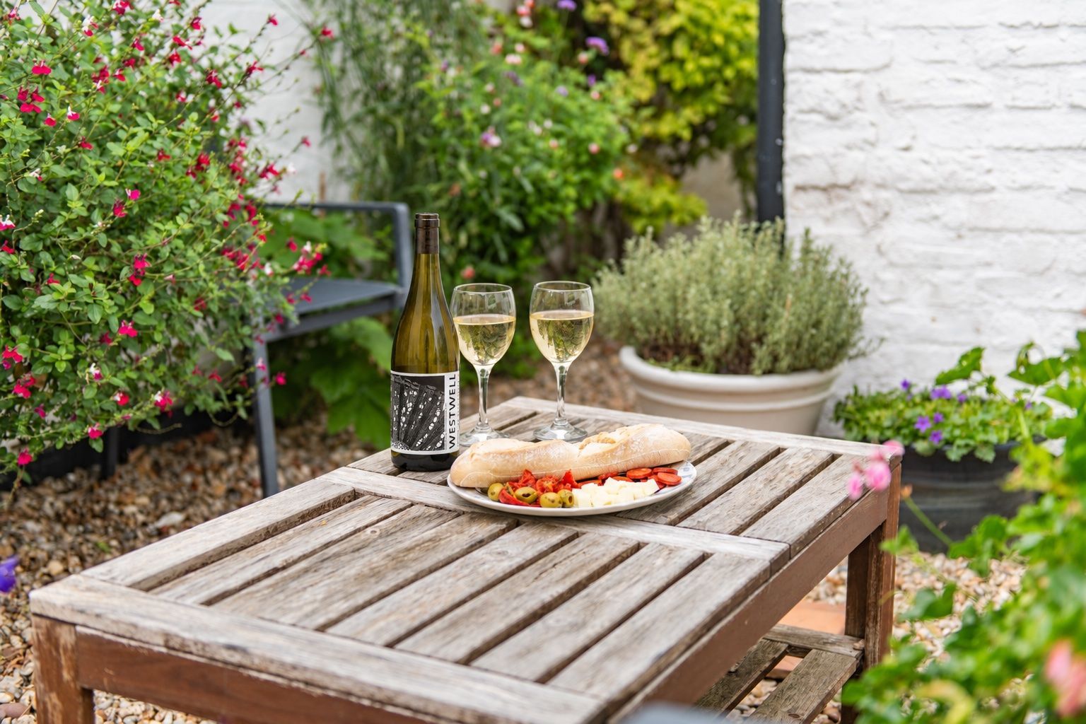 A wooden table with a bottle of wine, two glasses, and a plate of food.